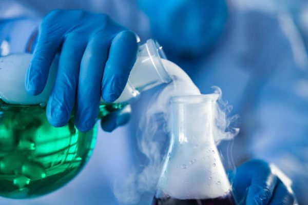 Close up of unrecognizable scientist pouring smoke from a beaker with green liquid in laboratory.